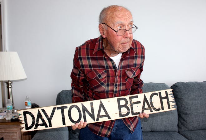 Roy Nickerson, 97, holding a sign he took off a tree on his first visit to Daytona Beach in 1937 when he was 17. He returned it this week, saying with a smile, "We looked it up, the statue of limitations is up." [News-Journal/Nikki Ross]