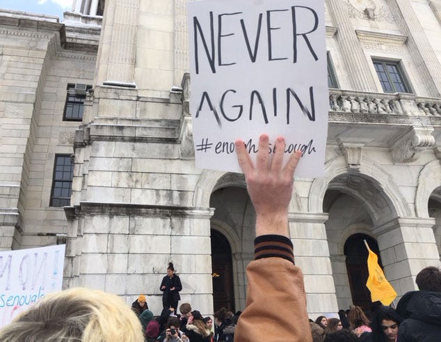 A protester at the State House Wednesday held a sign that reads, "Never Again #EnoughIsEnough". Hundreds of students marched to Smith Hill to protest gun violence, part of a national walkout day.