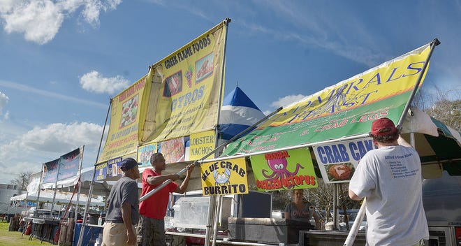 Shiva Locham, Patrick Tye and Shane Lowery raise a sign over their food booth at the St. Augustine Lions Seafood Festival. [PETER WILLOTT / THE RECORD]
