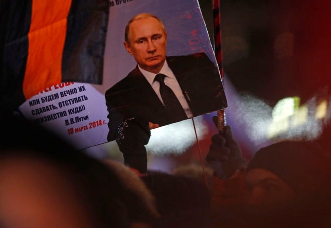 A person holds a banner of Russian President Vladimir Putin in Manezhnaya square, near the Kremlin in Moscow on Sunday. Putin handily won a fourth term as Russia's president, adding six more years in the Kremlin for the man who has led the world's largest country for all of the 21st century. [Pavel Golovkin/The Associated Press]