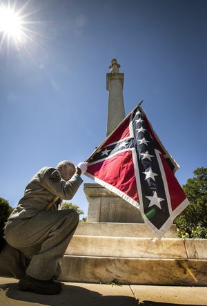 H.K. Edgerton, president of Southern Heritage 411, dressed in a Confederate soldier uniform, held a Confederate flag recently at the statue in Munn Park. The city has narrowed the number of possible relocation sites to two, and the move could cost $225,000.