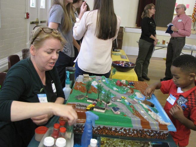 Hollie Greer, environmental specialist at the Alachua County Environmental Protection Department, uses a “Watershed Enviroscape” to teach 6-year-old Brian Dikes about stormwater pollution during the “Busting Myths About Energy Conservation” community forum. The enviroscape is an interactive stormwater pollution model depicting a town. [Photos by Aida Mallard/Special to the Guardian]