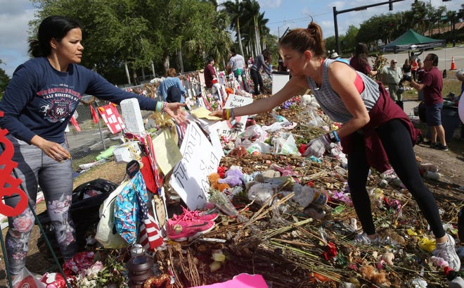 Patricia Padauy passes a handwritten note to her friend Sharamy Angarita as they clean and sort out items at the memorial site of Padauy's son Joaquin Oliver on Wednesday in Parkland. Volunteers, students and parents were sorting items left at the memorial sited for the 17 students and faculty killed at Marjory Stoneman Douglas High School on Valentine's Day. Flowers and plants will be composted while all other items will catalogued and saved. [Marta Lavandier/The Associated Press]