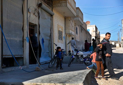 Syrian residents gather next of damaged shops, at the scene where an explosion on Thursday hit a U.S.-led coalition vehicles, killing an American and a Briton soldier, in Manbij town, north Syria, Saturday, March 31, 2018. The explosion on Thursday was the first to hit members of the U.S.-led coalition who have deployed to Manbij months after the town was liberated from Islamic State militants in 2016. An improvised explosive device went off during an operation against a known member of the Islamic State group in this mixed Arab and Kurdish town, the U.S-led Coalition said in a statement Saturday. (AP Photo/Hussein Malla)