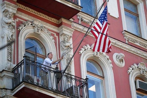 A consulate employee lifts up the U.S. flag at the U.S. consulate in St.Petersburg, Russia, Saturday, March 31, 2018. The flag was flown at half-mast to mourn victims of Kemerovo fire killing 64 people. Russia announced the expulsion of more than 150 diplomats, including 60 Americans, on Thursday and said it was closing a U.S. consulate in retaliation for the wave of Western expulsions of Russian diplomats over the poisoning of an ex-spy and his daughter in Britain, a tit-for-tat response that intensified the Kremlin's rupture with the United States and Europe. (AP Photo/Dmitri Lovetsky)
