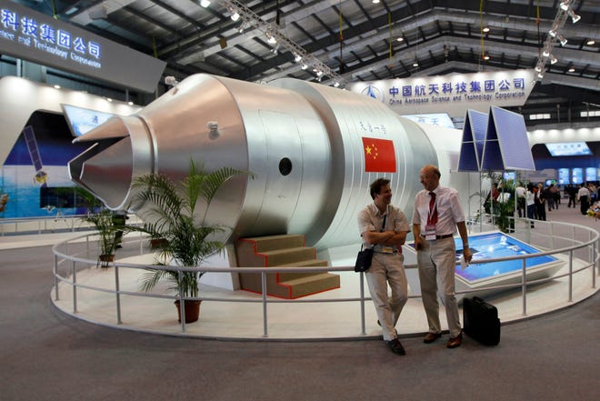 FILE - In this Nov. 16, 2010 file photo, visitors sit beside a model of China's Tiangong-1 space station at the 8th China International Aviation and Aerospace Exhibition in Zhuhai in southern China's Guangdong Province.China's defunct Tiangong 1 space station mostly burned up on re-entry Monday into the atmosphere over the central South Pacific, Chinese space authorities said.  [AP Photo/Kin Cheung, File]