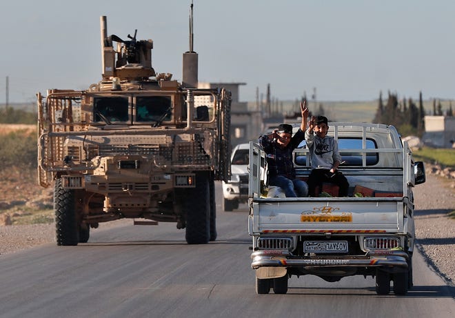 FILE -- In this Saturday, March 31, 2018 file photo, Syrian boys, right, sit on a pickup truck as they travel next to a U.S. vehicle, on a road leading to the tense front line with Turkish-backed fighters, in Manbij, north Syria. President Donald Trump expects to decide "very quickly" whether to remove U.S. troops from war-torn Syria, saying their primary mission was to defeat the Islamic State group and "we've almost completed that task." (AP Photo/Hussein Malla, File)