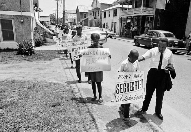 Dr. Martin Luther King, Jr. gives Eric James a pat on the back as they walk with a group of children down Washington Street in Lincolnville in St. Augustine toward a civil rights protest around the Plaza de la Constitucion on June 10, 1964. James, who now lives in New Jersey, said King was trying to reassure him that he would be safe during the march. [ASSOCIATED PRESS/FILE]