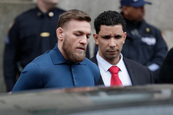 UFC star Conor McGregor, left, is led by an official to an unmarked vehicle while leaving the 78th Precinct of the New York Police Department, Friday. McGregor is facing criminal charges in the wake of a backstage melee he allegedly instigated that has forced the removal of three fights from UFC's biggest card of the year. [AP Photo/Julio Cortez]