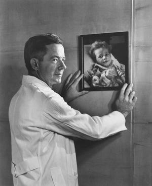 This photo of Dr. Alfred Blalock hanging a picture of a child on his wall was done to commemorate the 1,000th “blue baby” operation. [Photo by Yousuf Karsh]