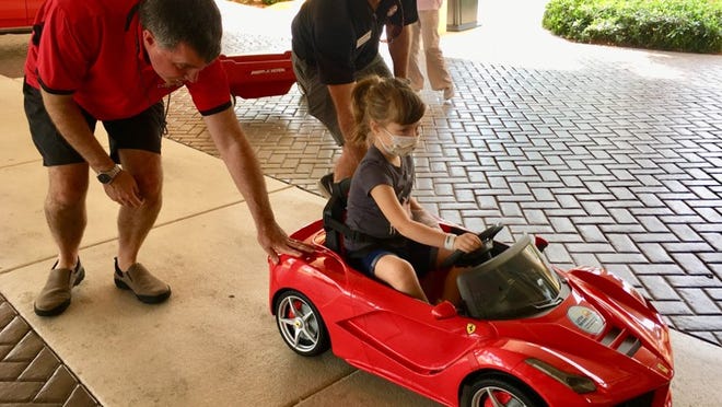 Brian Murphy (left) and Craig Kelley (center in black) roll a mini-Ferrari convertible carrying 5-year-old Abigail Sporke into Palms West Hospital on Saturday, April 7, 2018. Murphy and Kelley are with nonprofit Little Smiles, which donated the car to the hospital's pediatric patients. (Photo by Lulu Ramadan/Palm Beach Post)