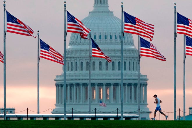 FILE - In this Sept. 27, 2017, file photo, a early morning runner crosses in front of the U.S. Capitol as he passes the flags circling the Washington Monument in Washington. Congress returns from spring break Monday, April 9, 2018, scrambling to compile a to-do list that will satisfy a president they desperately need to be touting their achievements, not undermining them, as they prepare to hit the campaign trail. (AP Photo/J. David Ake, File)