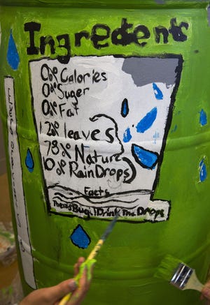 Students paint a sign on the side of their rain barrel poking fun at a soda can ingredient label. (Chris Pietsch/The Register-Guard)