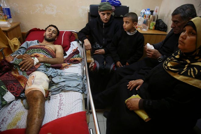 In this Monday, April 9, 2018 photo, Raed Jadallah, a Palestinian 25-year-old surfer, lies on a bed as his father, mother and brothers visit him, at the Shifa hospital in Gaza. Jadallah is among the nearly 1,300 people that Palestinian health officials said have been shot and wounded by Israeli soldiers during mass border protests over the past two weeks. The casualty figures are at the heart of an intensifying debate over the military's open-fire orders. (AP Photo/Adel Hana)
