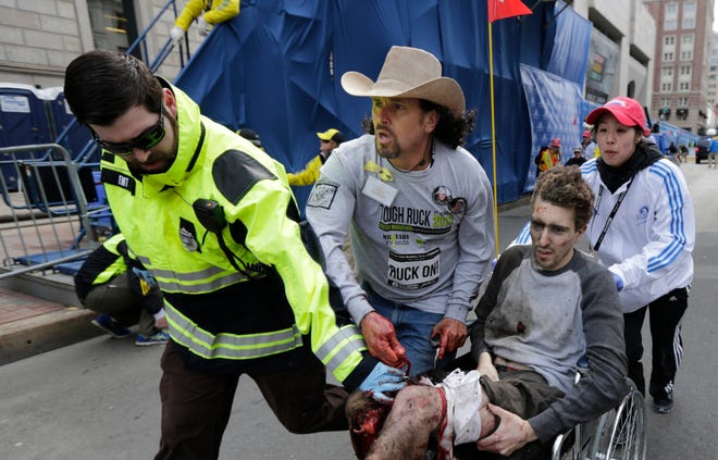FILE - In this April 15, 2013, file photo, Boston Marathon bombing survivor Jeff Bauman is helped by Emergency Medical Services EMT Paul Mitchell, left, Carlos Arredondo, center, and Devin Wang, right, after he was injured in one of two explosions near the finish line of the Boston Marathon in Boston. Arredondo now volunteers with the Red Cross, and his family foundation works to prevent military-related suicides. He is preparing to run in his first Boston Marathon on April 16, 2018. (AP Photo/Charles Krupa, File)