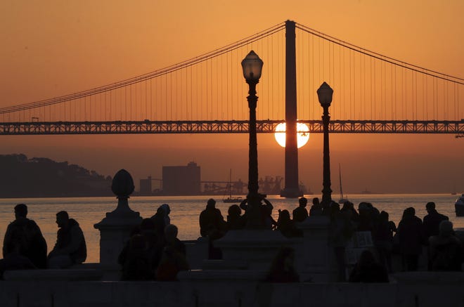 People gather at Comercio Square in Lisbon, Portugal, to watch the sun set behind the April 25th Bridge. A new tour company called Off the Grid, which asks participants to put their cellphones away, is launching with a trip to Lisbon in July. [AP file / Armando Franca]