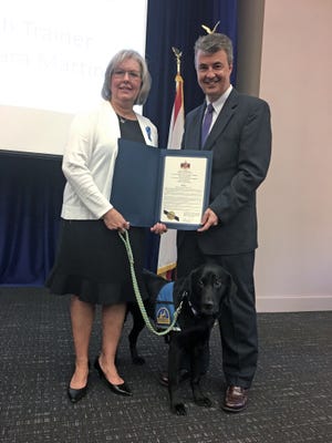 Alabama Attorney General Steve Marshall on Friday presents a proclamation to Tamara Martin, a forensic interviewer at Child Protect Children’s Advocacy Center, and Willow, a black Labrador Retriever who helps ease the stress of children and adult victims of crime. [Photo by the Alabama Attorney General's Office]