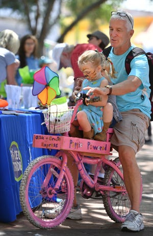 Charlie Hull takes his granddaughters, Olivia, 2, and Gracie, 4, for a ride on their 'Poppie Powered' bicycle at the Earth Day celebration at Five Point Park on Friday. Sarasota County and the City of Sarasota co-hosted the Earth Day event which included information tables from local sustainability organizations and government agencies to help people take simple steps to reduce their carbon footprint. [HERALD-TRIBUNE STAFF PHOTO / MIKE LANG]