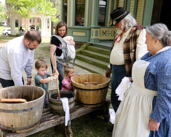 Dressed as a Civil War hospital laundress, Susan Trisler along with Harold Trisler watch as the May family, from left, Jeremy, Warren, 3, Bailey, 2, infant Maddox and Sarah, try their hand at how it was to wash clothes during the Civil War era Saturday, April 21, 2018, during the Civil War-era Union hospital re-enactment at the historic Clayton House. [JAMIE MITCHELL/TIMES RECORD]