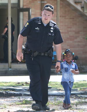 An officer escorts a little girl out of Eagle Nest Academy. All schools in the area around the Cove were on lockdown on Monday afternoon after a white male attempted to rob the Eagles Nest Academy. [PATTI BLAKE/THE NEWS HERALD]