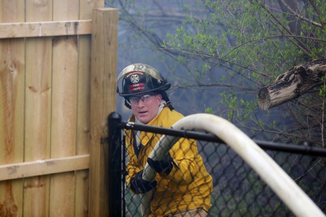 Burlington firefighter Todd Van Scoy pulls a hose over a fence Friday as members of the Burlington and West Burlington fire departments battle a brush fire along BNSF railway right-of-way property between Vogt Street and Aldo Leopold Middle School. [John Lovretta/thehawkeye.com]