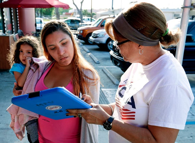 In this April 12, 2018 photo, Michelle Ortiz, who was born in New York to Puerto Rican parents and recently moved to Florida, holds her daughter as she registers to vote with the help of volunteer Carmina Redonet, right, in Orlando, Florida. Political operatives, pollsters and politicians in at least four states are working hard right now to find Puerto Ricans who are eligible to vote and whose party affiliation may be up for grabs. (AP Photo/John Raoux)