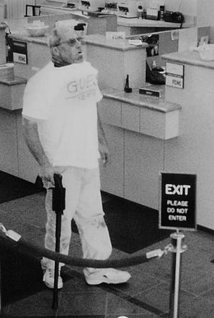 Brian Wells is seen inside the PNC bank in Summit Towne Centre in Erie, Pa., on August 28th, 2003. In this FBI hand out of the surveillance images shot during the bank robbery. Wells is carrying the cane gun and wearing the collar bomb which is protruding from his shirt. This image was taken prior to him receiving money from the teller. In his mouth is a sucker that he picked up while waiting to approach the teller as stated by the FBI. Wells would later die from injuries suffered when the collar bomb detonated. (AP Photo by Rich Forsgren/Erie Times-News) FBI HANDOUT