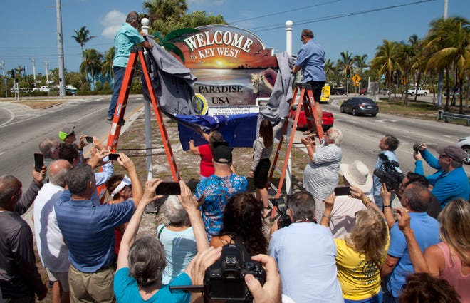 In this photo provided by the Florida Keys News Bureau, Rotary Club of Key West President Albert Gonzalez, left, and sign artist Carl Reid, right, unveil a "Welcome to Key West" sign Tuesday, May 1, 2018, in Key West, Fla. Valued at $8,000, the sign fell during Hurricane Irma in September 2017 and subsequently was picked up by a motorist. A Key West Police Department investigation led to its recovery in Fort Myers Beach, Fla. (Carol Tedesco/Florida Keys News Bureau via AP)