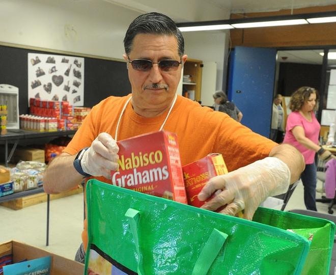 Carlos Costa, member of the Food Pantry Board of Directors, packs food for a client at the pantry. [DAVE SOUZA/HERALD NEWS]