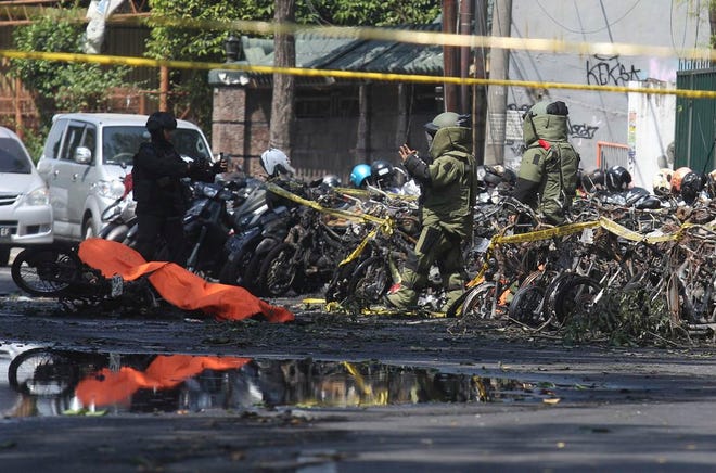 Members of police bomb squad inspect the wreckage of motorcycles at the site where an explosion went off outside a church in Surabaya, Indonesia. Almost simultaneous attacks including one by a suicide bomber disguised as a churchgoer targeted churches in Indonesia's second largest city of Surabaya early Sunday, killing a number of people and wounding dozens, police said. [Trisnadi/The Associated Press]