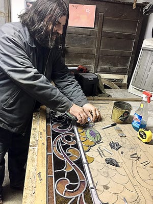 Following the design of the windows, Shane O'Brien carefully attaches a piece of the original glass, which is held together by flexible strips of leading and solder.
