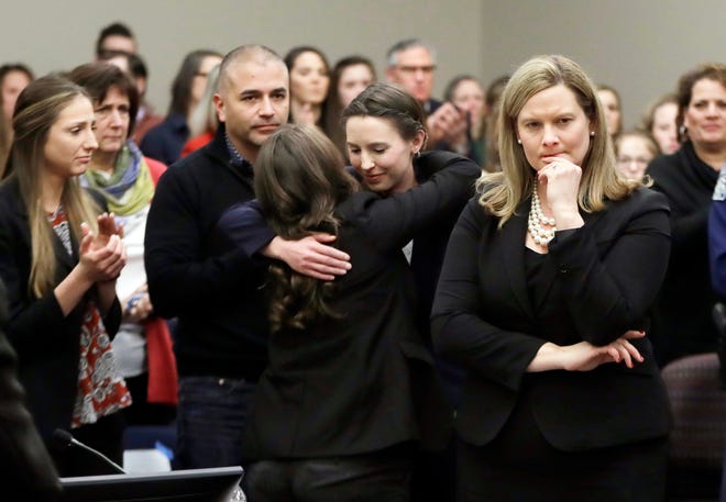 FILE - In this Jan. 24, 2018, file photo, former gymnast Rachael Denhollander, center, is hugged after giving her victim impact statement during the seventh day of Larry Nassar's sentencing hearing in Lansing, Mich. At right is Assistant Attorney General Angela Povilaitis. Michigan State University announced Wednesday, May 16, 2018, that it has reached a $500 million settlement with hundreds of women and girls who say they were sexually assaulted by sports Nassar in the worst sex-abuse case in sports history. (AP Photo/Carlos Osorio, File)
