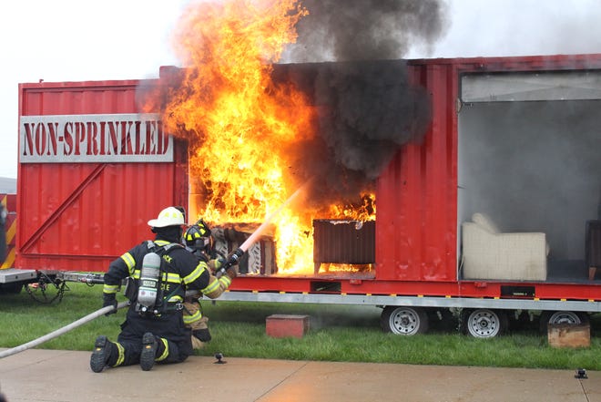 Holland and Saugatuck firefighters put out a fire that has destroyed a mock living room on Saturday, May 19. On the right side of the demonstration trailer, a similar living room fire was put out by a home fire sprinkler system in under two minutes. [Audra Gamble/Sentinel staff]
