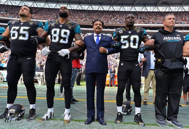 Jacksonville Jaguars team owner Shad Khan (center) and head coach Doug Marrone stand united arm-in-arm with players Brandon Linder (65) Marcedes Lewis (89) and Telvin Smith (50) on the sideline during the singing of the American national anthem before kick-off against the Baltimore Ravens in an NFL game Sunday, September 24, 2017 in London, U.K. (Rick Wilson/Jacksonville Jaguars)