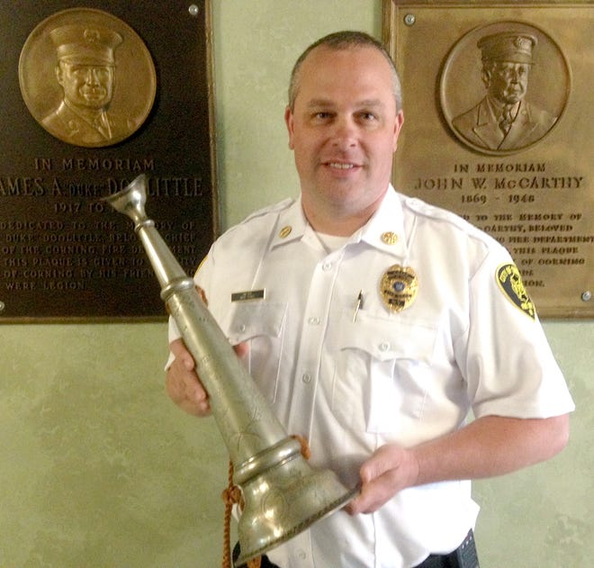 Corning Fire Chief Brad Davies poses with the 1850s Pritchard Hose Company metal trumpet Tuesday in front of memorials to past Fire Chiefs James Doolittle, left, and John McCarthy. [SHAWN VARGO/THE LEADER]