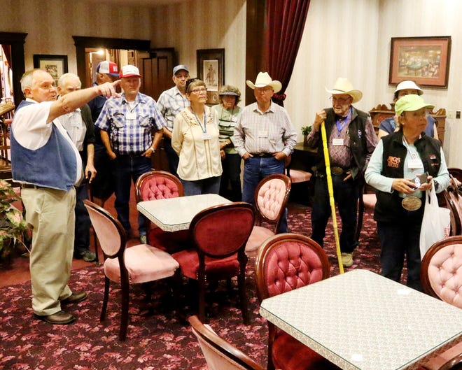 Fort Smith Visitor Center volunteer Larry Woodham, left, points out a few of the 19th century clothing items on display Tuesday, May 22, 2018, in the parlor of Miss Laura's during a tour with guests from the Western Livestock Journal group. More than 150 livestock owners and ranchers rode in three buses from Bentonville to Fort Smith as part of their tour of Western-themed locations and visited the Fort Smith Musuem of History, Fort Smith National Historic Site and Miss Laura's before busing to the Belle Point Ranch for lunch. [JAMIE MITCHELL/TIMES RECORD]
