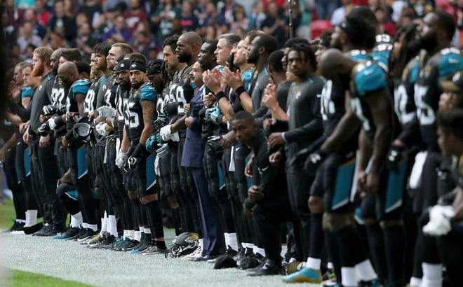 Jacksonville Jaguars owner Shahid Khan, center, joined arms with players as some kneel down during the playing of the U.S. national anthem before an NFL game in London last September. [AP File Photo/Tim Ireland]
