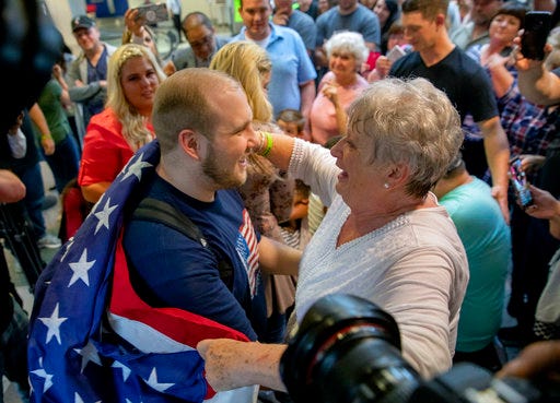 Josh Holt, left, is draped in an American flag by his grandmother Linda Holt upon returning to Salt Lake City on Monday, May 28, 2018, as he was freed this weekend after being held in a Venezuelan jail for nearly two years. He returned home to Salt Lake City on Monday night after getting medical care and visiting President Donald Trump in Washington. (AP Photo/Kim Raff)