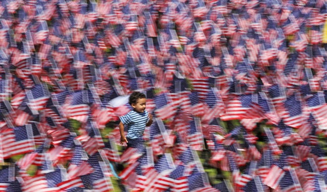 Christian Dacosta, 3, of Providence, runs through the field by The Temple to Music at Providence's Roger Williams Park where flags are set up at the Boots on the Ground for Heroes Memorial. The memorial features 6,920 combat boots, each adorned with flags and a name placard honoring U.S. soldiers killed in action since 9/11. It will be open through Monday, Memorial Day. [The Providence Journal/Steve Szydlowski]