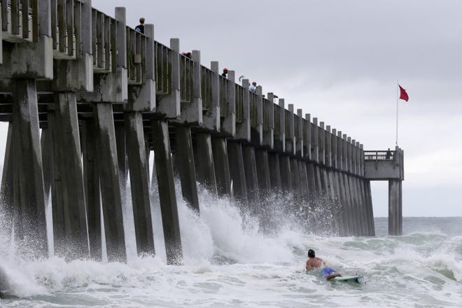 A surfer makes his way out into the water as a subtropical approaches on Monday in Pensacola. [AP Photo/Dan Anderson]