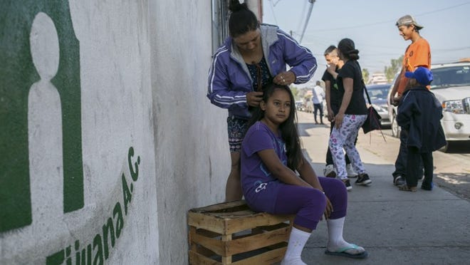 Orfa Marin of Honduras, braids the hair of Rosemarie Gonzalez, 10, from El Salvador, in Tijuana, Mexico in April. The two were among hundreds of migrants who traveled en masse across Mexico. (Meghan Dhaliwal/The New York Times)