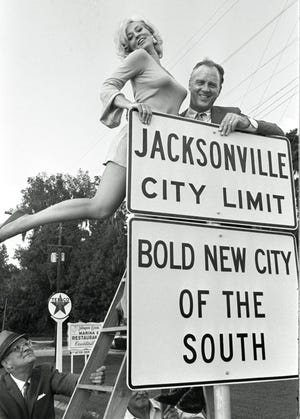 Actress Lee Meredith helped Mayor Hans Tanzler raise the new city limits sign after consolidation in this iconic 1968 file photo. Meredith was in town playing the role of The Blonde in "Champagne Complex" at the Alhambra Theatre. A Call Box reader wants to know the identity of the man in the lower left corner steadying the ladder. [Lou Egner/Florida Times-Union]