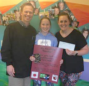 Emma Johnston, center, of Meadowbrook Middle School displays the winning essay about "My Favorite Teacher" in a contest sponsored by Dean Orthodontics. Emma won a $100 Visa gift card and her favorite teacher, Carrie Winland, right, won $500 for her classroom. Pictured with Emma and Winland is Dr. Jared Dean.