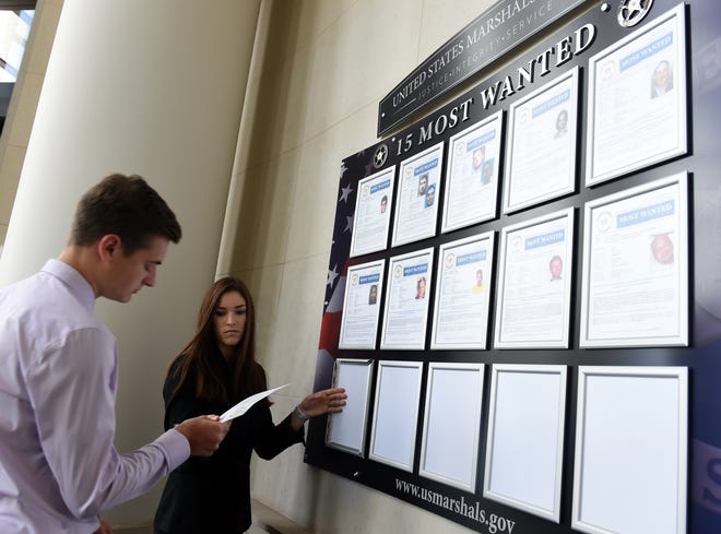 Kenzie Myers and Cooper Devins, interns with the U.S. Marshals Service in Cleveland, adjust the 15 Most Wanted display.