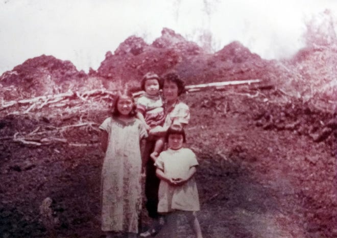 This 1955 photo provided by Rosemary Kawamoto shows her, at 9, left, her mother Mildred Nii holding her sister Carol, 3, with her sister Ethel Jane, 5, right, posing in front of a still-smoking cinder cone after an eruption on their family farm at Pahoa on the island of Hawaii. Lava spared their house, but her family never moved back because her mother, a city girl from Honolulu, objected. The family moved to Hilo, the largest town on the Big Island, and sold the farm. (Courtesy Rosemary Kawamoto via AP)