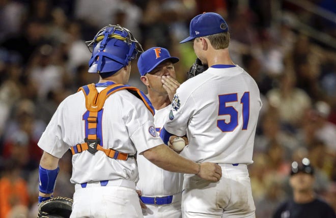Florida coach Kevin O'Sullivan covers his mouth as he talks to pitcher Brady Singer (51) and catcher Jonah Girand in the fifth inning Sunday of the College World Series game against Texas Tech in Omaha, Neb. [Nati Harnik/Associated Press]