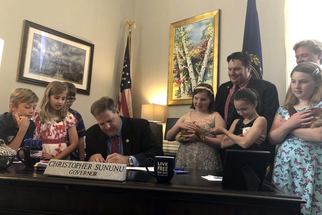 Republican Gov. Chris Sununu signs a bill in Concord, N.H., Monday, June 18, 2018, designating the New Hampshire Red as the official state poultry of New Hampshire. The governor was joined by Canaan Elementary School students who proposed the bill, and two chickens named Peachy and Rusty. [AP Photo/Holly Ramer]
