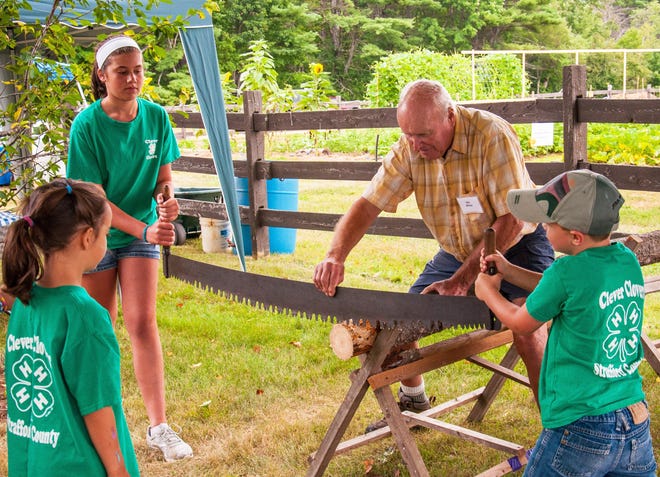 WWW Festival volunteer and New Durham resident Bill Malay helps kids use a crosscut saw to cut a 'tree cookie' slice of a pine log duing last year's festival. This year's festival is slated for Aug. 11. [Kate Wilcox photo]
