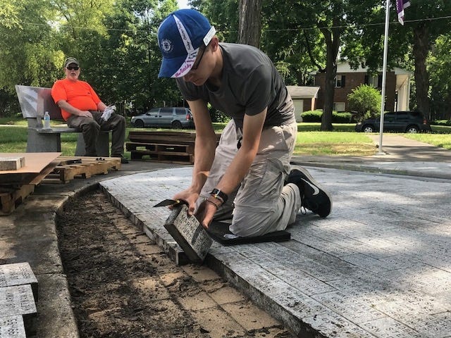 William Trent, a Boy Scout from troop 1102, works on removing bricks from the west side of the memorial at Veteran’s Park in Lincoln. Michael Downen, who was taking turns pulling the bricks up, rests on the bench in the background. [Photo by Jean Ann Miller/The Courier]