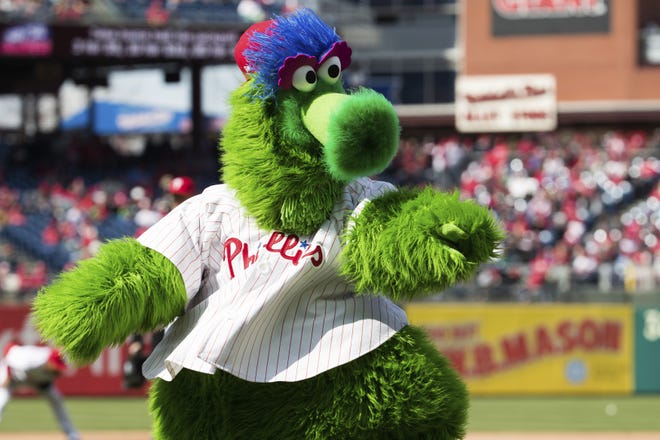 In this April 5, 2018 photo, The Phillie Phanatic reacts prior to the first inning of a baseball game against the Miami Marlins in Philadelphia. Kathy McVay says she was at the Monday, June 18, Phillies game when the team’s mascot, the Phillie Phanatic, rolled out his hot dog launcher. McVay was sitting near home plate and all of a sudden she says a hot dog wrapped in duct tape struck her in the face. She left the game to get checked out at a hospital, and she says she has a small hematoma. The Phillies apologized to McVay Tuesday and the team has offered her tickets to any game. [AP Photo/Chris Szagola]